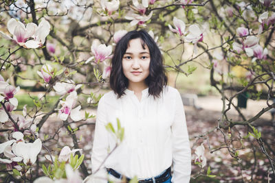 Happy asian young woman under the blooming magnolia tree, smiling