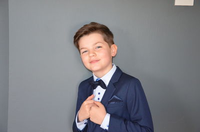 Portrait of boy in full suit standing against gray background