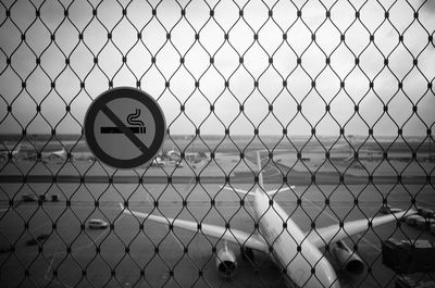 Close-up of signboard on chainlink fence at airport against sky