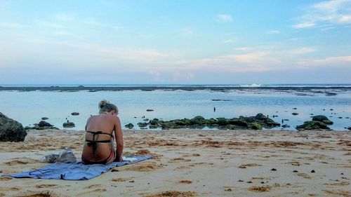 Rear view of man sitting on beach against sky