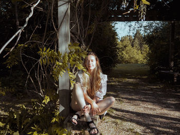 Portrait of young woman sitting on tree in forest