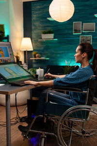 Side view of artist sitting on wheelchair while working at home