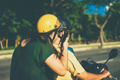 Rear view of woman holding mobile phone while sitting behind man riding motor scooter