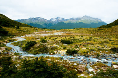 Scenic view of stream by mountains against sky