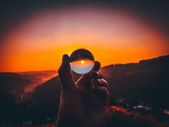 Man photographing orange camera against sky during sunset