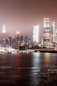 Illuminated city by river against sky at night