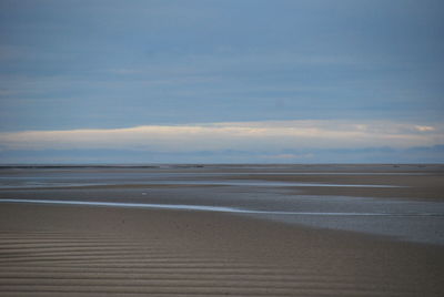 View of calm beach against cloudy sky