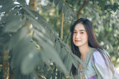 Portrait of smiling young woman standing by trees