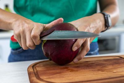 Woman cutting a mango in the kitchen on a wooden board