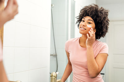 Teenage girl applying cream reflecting on mirror in bathroom