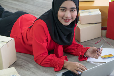 Portrait of smiling young woman using phone while sitting on table