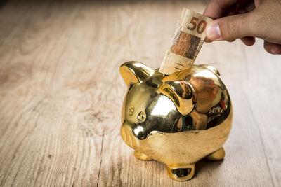 High angle view of person holding paper currency over piggy bank on table