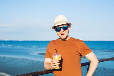 Portrait of woman wearing sunglasses while standing at beach against sky