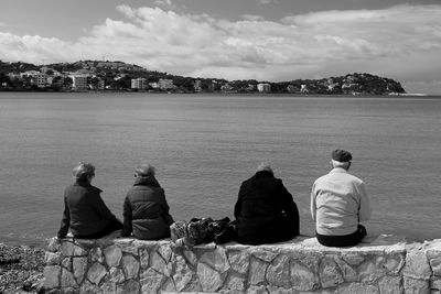 Rear view of people relaxing on retaining wall against sea