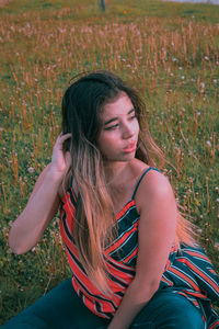 Young woman looking away while sitting on land