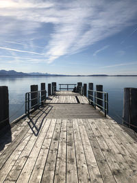 Wooden jetty leading to pier over sea against sky