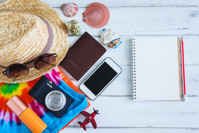 Directly above shot of travel equipment with notebook and pen on wooden table