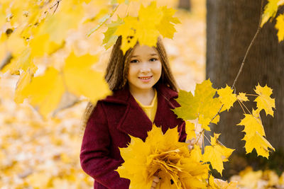 Portrait of young woman standing by tree during autumn