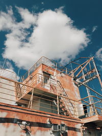 Low angle view of crane by building against sky