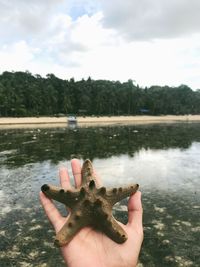 Close-up of hand holding water against lake