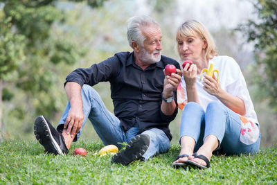 Full length of senior man with woman holding apple at park