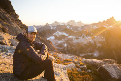 Portrait of man sitting on rock at sunset in mountains.