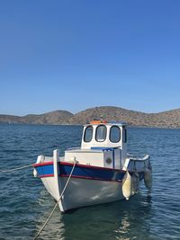 Boat moored in sea against clear blue sky