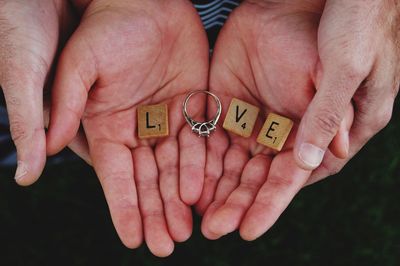 Cropped hands of couple holding wooden blocks with engagement ring making love text