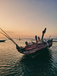Fishing boat moored in sea against sky during sunset