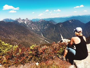 Rear view of woman sitting on mountain against sky