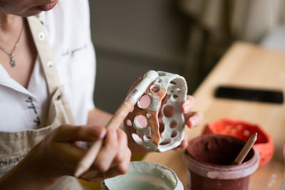 Close up view of female potter wearing apron using glaze brush to paint on pot