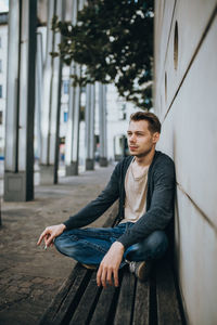 Young man looking away while sitting on wall