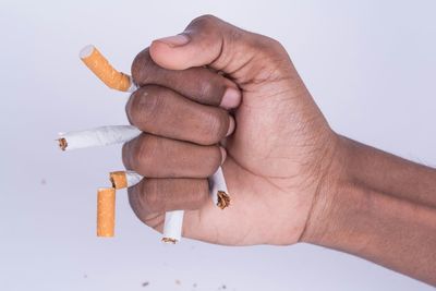 Close-up of hand holding cigarette over white background