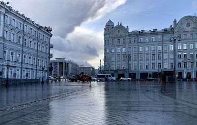 Wet street amidst buildings in city