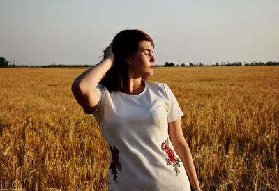 Young woman with hand in hair standing against field