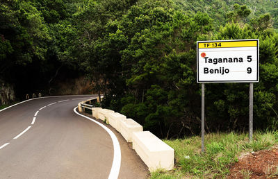 Text on sign board by road against trees