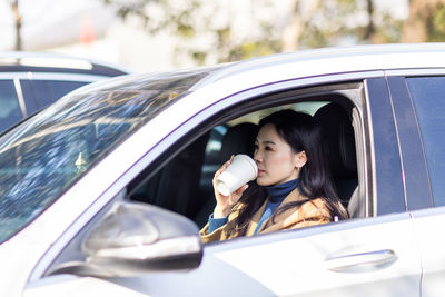Beautiful woman drinking coffee while sitting in car