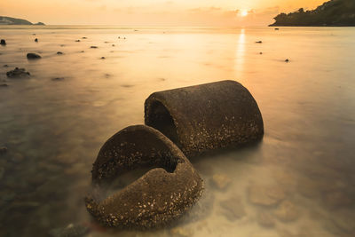 Stones on rock at beach against sky during sunset