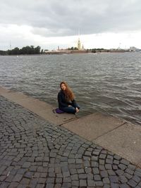 Woman sitting on river against sky in city