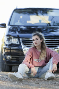 Portrait of teenage girl sitting against car