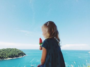 Side view of girl holding popsicles standing against sky