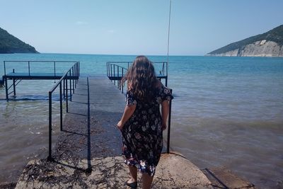 Rear view of woman standing at beach against sky