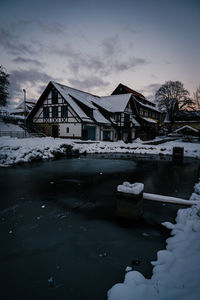 Houses by river against sky during winter