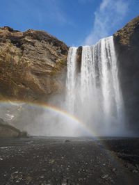 Scenic view of waterfall against rainbow in sea