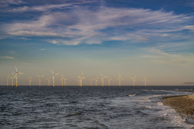 Wind turbines on sea shore against sky during sunset