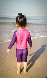 Rear view of boy standing on beach against sky