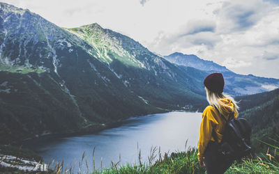 Rear view of woman standing on mountain by river against sky