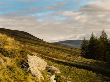 Scenic view of green mountains against cloudy sky on sunny day