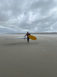 Rear view of woman standing at beach against sky