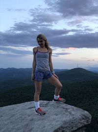 Full length portrait of young woman standing on mountain against sky